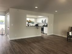 an empty living room with hard wood flooring and white walls in the kitchen area