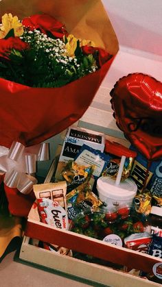 a red heart shaped balloon sitting on top of a box filled with flowers