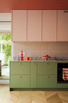 a kitchen with pink and green cabinets, marble counter tops and wooden flooring that has chevroned parquet pattern on it