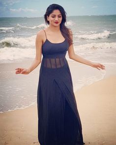 a woman standing on top of a sandy beach next to the ocean with her arms outstretched