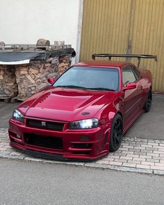 a red sports car parked in front of a garage with wood stacked on the ground