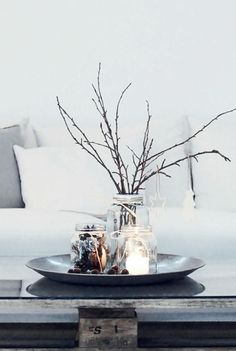 a glass vase with branches in it sitting on a table next to pillows and pillows