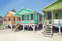 several colorful beach huts on the sand with stairs leading up to them