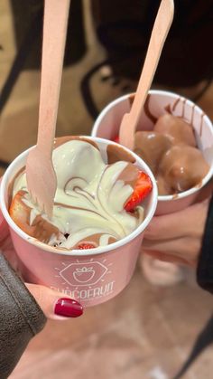 two ice creams with strawberries and chocolate on top are being held by someone's hand