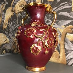 a red and gold vase sitting on top of a table next to a floral wallpaper