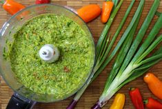 a blender filled with green liquid surrounded by vegetables and carrots on a table