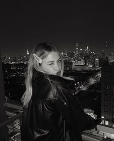 a woman standing on top of a tall building next to a city skyline at night