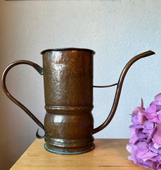 a metal watering can sitting on top of a wooden table next to purple hydrangeas