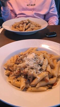 a woman sitting at a table in front of two plates of pasta with meat and cheese