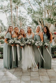 a group of women standing next to each other wearing dresses and holding bouquets in their hands