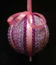 a pink ornament with beads and a ribbon on it's side, hanging from a black background