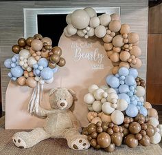 a teddy bear sitting in front of a balloon arch with balloons attached to the top