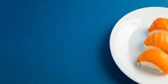 three pieces of sushi on a white plate against a blue background with copy space