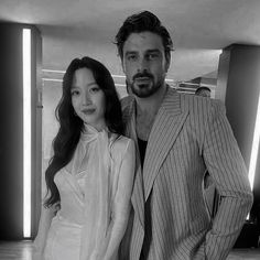 a man standing next to a woman in a white shirt and suit on top of a hard wood floor