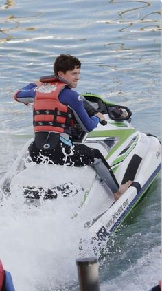 a young man riding on the back of a white and green jet ski while being pulled by a boat