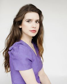 a woman with long brown hair wearing a purple shirt and posing for a photo in front of a white background