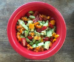 a red bowl filled with cucumbers, tomatoes and other vegtables