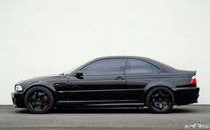 a black sports car parked in front of a white wall with red rims on it