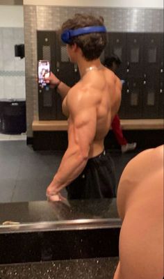 a shirtless man taking a selfie with his cell phone in a public restroom