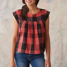 a woman standing in front of a wall wearing a red and black plaid top with ruffles