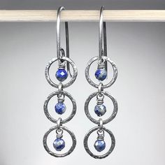 "These dangle earrings are created from genuine blue Lapis Lazuli gems and sterling silver.  The tiny natural stones are framed by a set of sterling silver circular rings.  I have created the rings by forming, soldering, and hammering them by hand.  The drops dangle from handmade sterling silver earwires.  The silver has been oxidized and polished to create an antique patina finish. Be sure to see all photos and video for size and color reference.   Lapis Lazuli: About 3.5mm Total Earring Length Sapphire Sterling Silver Hoop Earrings For Gift, Sapphire Dangle Earrings With Natural Stones, Sapphire Sterling Silver Hoop Earrings As Gift, Sapphire Dangle Jewelry With Natural Stones, Nickel Free Lapis Lazuli Round Jewelry, Blue Sterling Silver Hoop Earrings Nickel-free, Nickel Free Silver Lapis Lazuli Jewelry, Silver Dangle Hoop Earrings With Natural Stones, Blue Sterling Silver Hoop Earrings Nickel Free