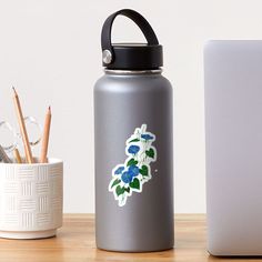 a silver water bottle with blue flowers on it next to a laptop and pencils