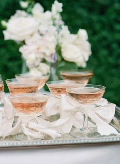 several glasses of wine on a tray with napkins and flowers in the back ground