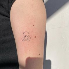 a small teddy bear tattoo on the left upper arm and lower arm, which has a tiny outline