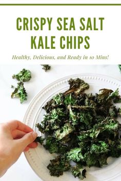 a white plate topped with kale chips on top of a table next to a hand