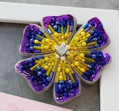 a purple and yellow flower brooch sitting on top of a white table next to a pink box