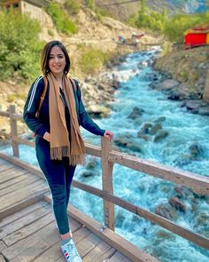 a woman standing on a wooden bridge next to a river with rapids in the background