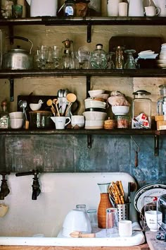 a kitchen sink filled with lots of dishes and utensils on top of a wooden shelf