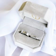 two wedding rings sitting in a box on top of a white cloth covered tablecloth