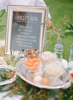 a table topped with plates filled with food next to a chalkboard sign that says omelet bar