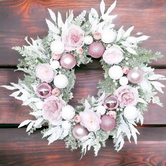 a wreath with pink and white flowers on a wooden surface, surrounded by greenery