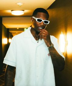 a man in white shirt and sunglasses standing next to a wall with lights on it