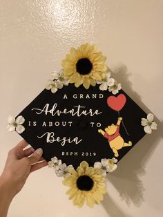 a graduation cap decorated with sunflowers and an air balloon is being held by a hand