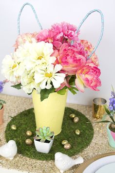 a yellow vase filled with pink and white flowers on top of a green table cloth