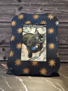 a black cat with blue eyes and yellow stars on it's face in a frame