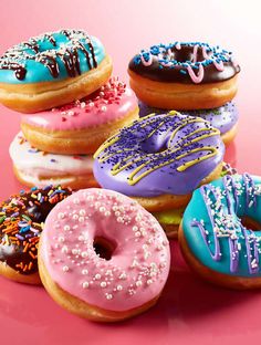 there are many donuts with different toppings on the pink surface and one has sprinkles