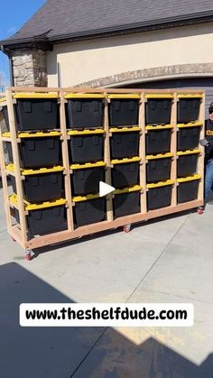 a man sitting on top of a wooden pallet next to black bins in front of a house