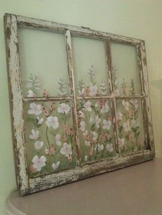 an old window frame with flowers painted on the outside is sitting on top of a table