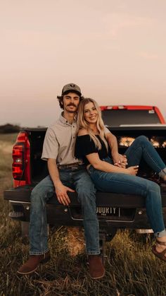 a man and woman sitting on the back of a pickup truck in an open field