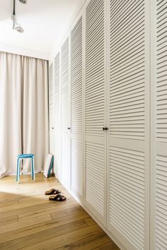 a room with white closets and wooden floors in front of a curtained window