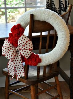 a wreath with red and white flowers on it sitting in front of a wooden chair