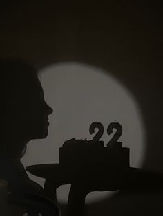 a woman holding a cake with the number twenty two on it in front of a dark background