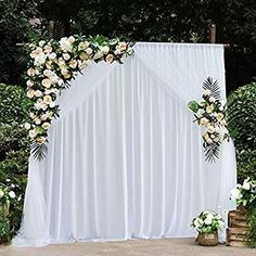 an outdoor wedding setup with white drapes and flowers on the side wall, along with greenery