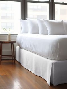 a bed with white sheets and pillows next to a window in a room that has wooden floors