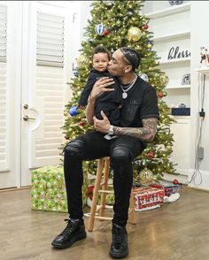 a man sitting in front of a christmas tree holding a small child on his lap