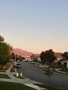 cars are parked on the street in front of houses with mountains in the back ground